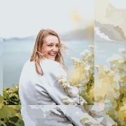 Een blond meisje met een grijze trui poserend voor de zee