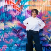 Een lachend getind meisje voor een kleurrijke muur 